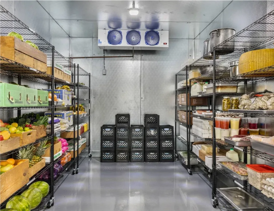 Walk-in cooler stocked with produce crates, dairy and pans on wire shelving